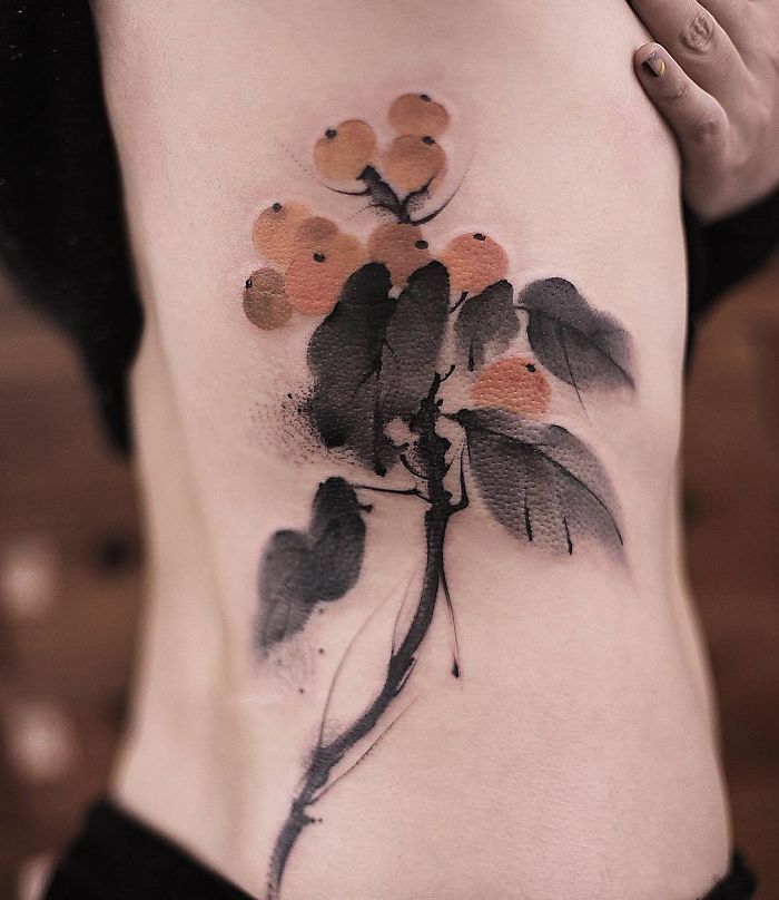 Watercolor tattoo by Chen Jie featuring delicate orange berries and leaves on a person's side.