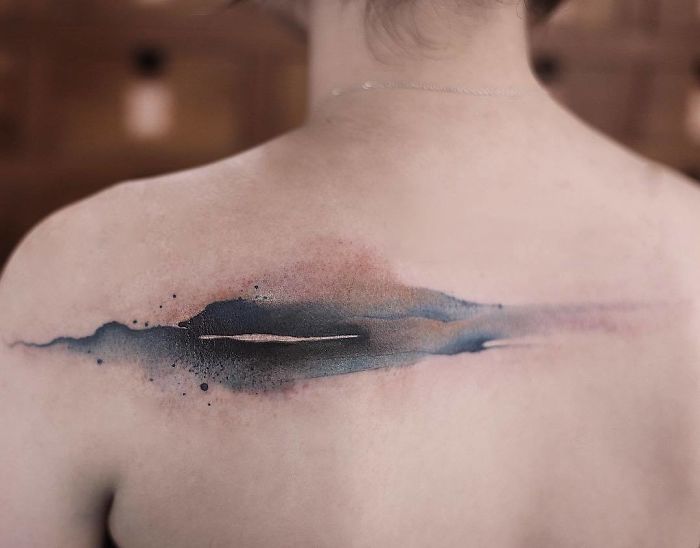 Watercolor tattoo in blue and pink tones on a person's shoulder, showcasing Chen Jie's artistic design.