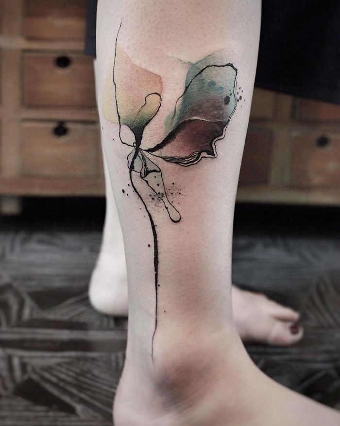 Watercolor tattoo with abstract butterfly design on leg, showcasing vibrant hues and delicate lines by artist Chen Jie.