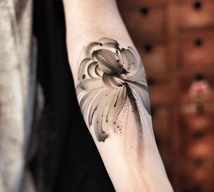 Watercolor tattoo on arm featuring abstract, floral design in soft black and grey hues.
