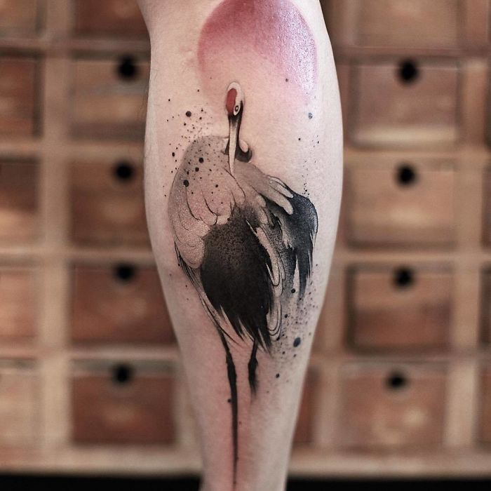 Watercolor tattoo by Chen Jie of a crane with a red sun on leg, featuring soft washes and delicate details.