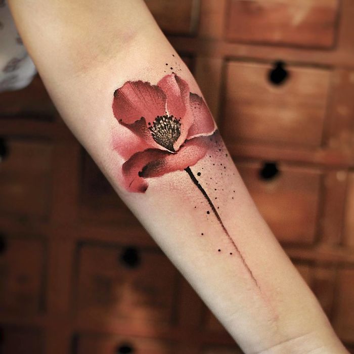 Watercolor tattoo of a red flower on an arm by Chen Jie.