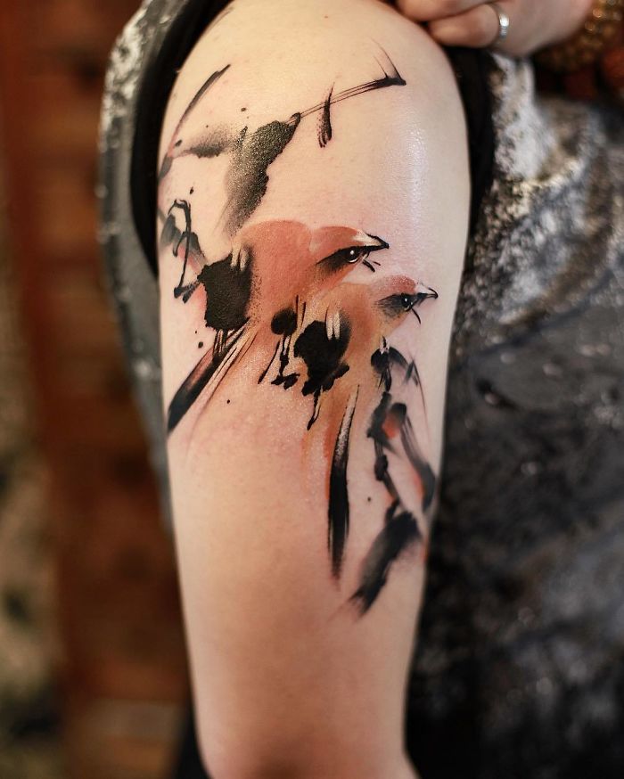 Watercolor tattoo by Chen Jie on an arm, featuring abstract black and red brushstroke designs.