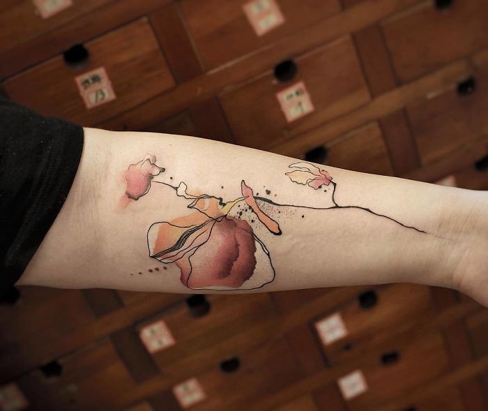 Watercolor tattoo by Chen Jie featuring delicate floral design on forearm.