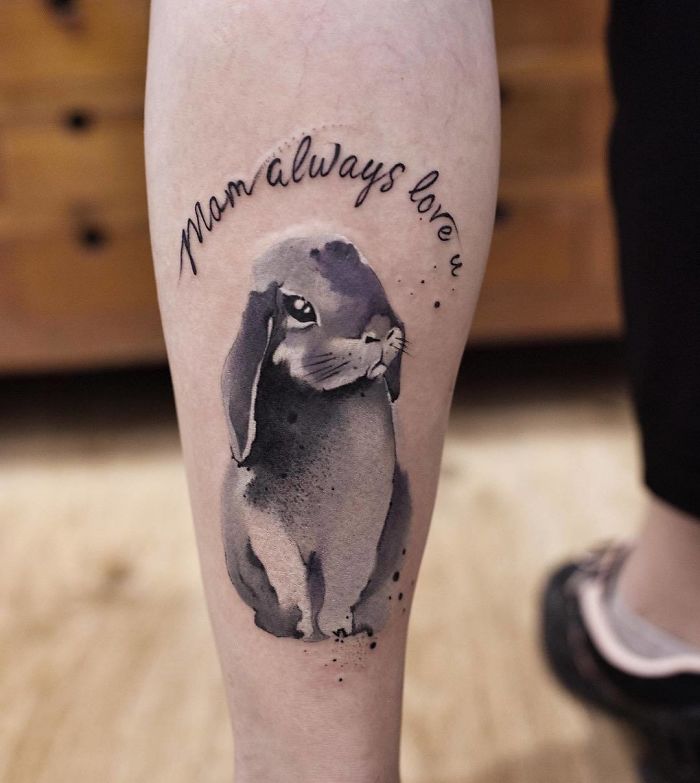 Watercolor tattoo by Chen Jie featuring a rabbit and the words "Mom always love u" on a person's calf.