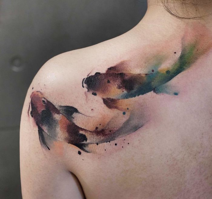 Watercolor tattoos featuring abstract fish design on a person's shoulder by artist Chen Jie.