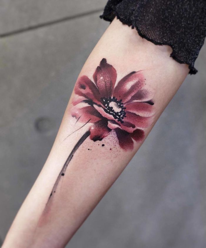 Watercolor tattoo of a red flower on a forearm, created in Chen Jie's signature style.