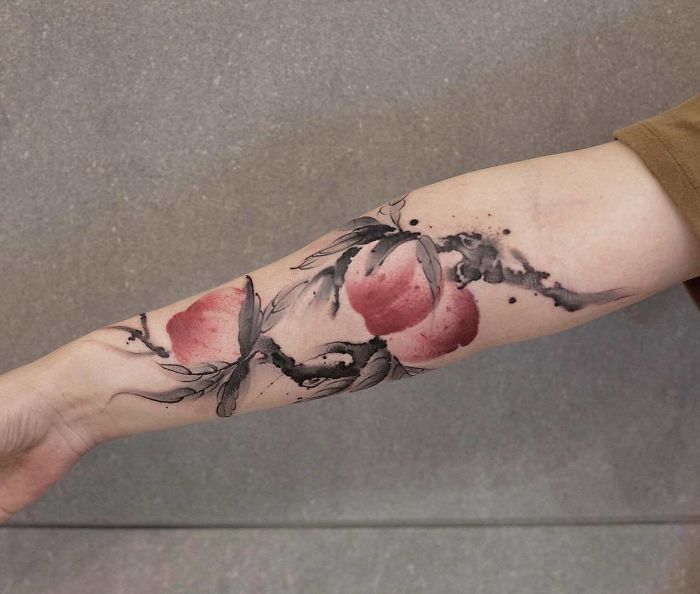 Watercolor tattoo of peaches and branches on forearm, showcasing Chen Jie's artistic style.