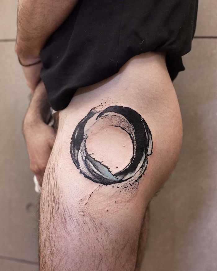 Watercolor tattoo by Chen Jie on thigh, depicting a circular design with abstract brush strokes.