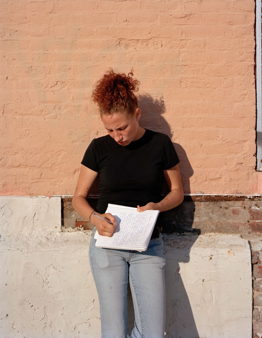 Portrait of Lauren posing near concrete wall and writing journal