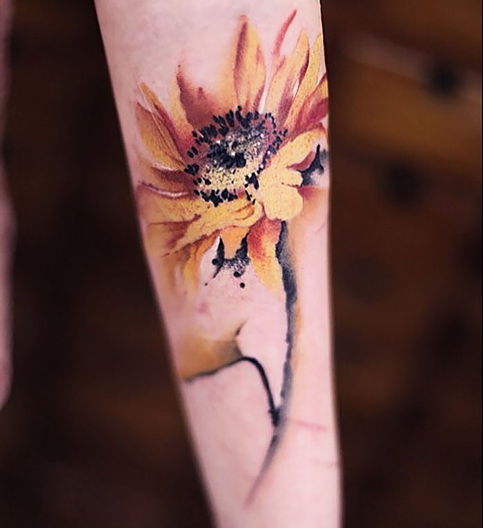 Watercolor tattoo of a sunflower by Chen Jie on a person's forearm, blending artistic colors for a soft look.