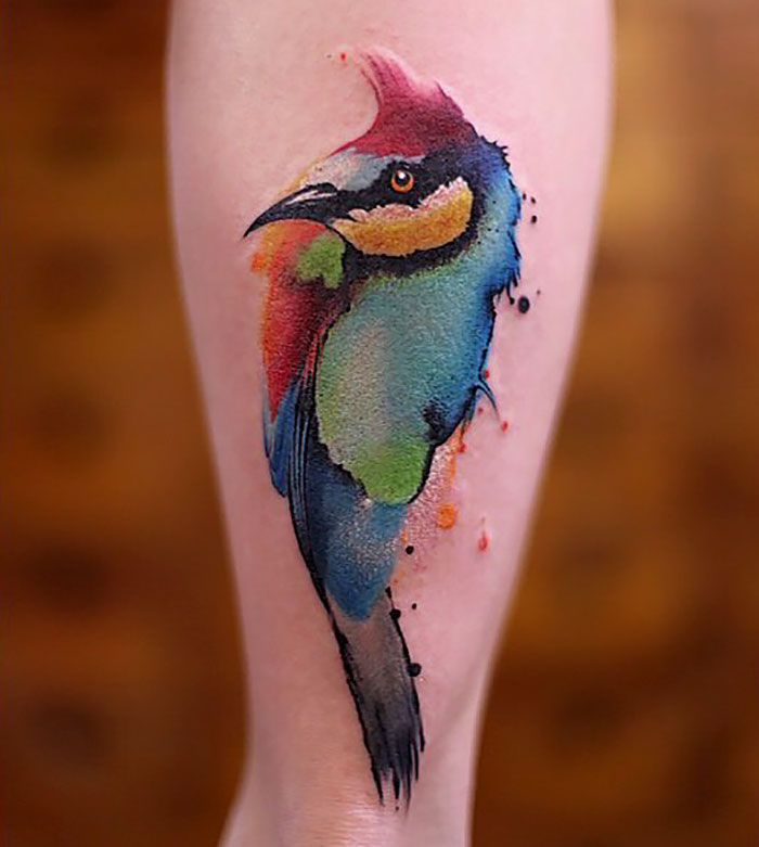 Watercolor tattoo of a colorful bird on skin, showcasing Chen Jie's artistic style.