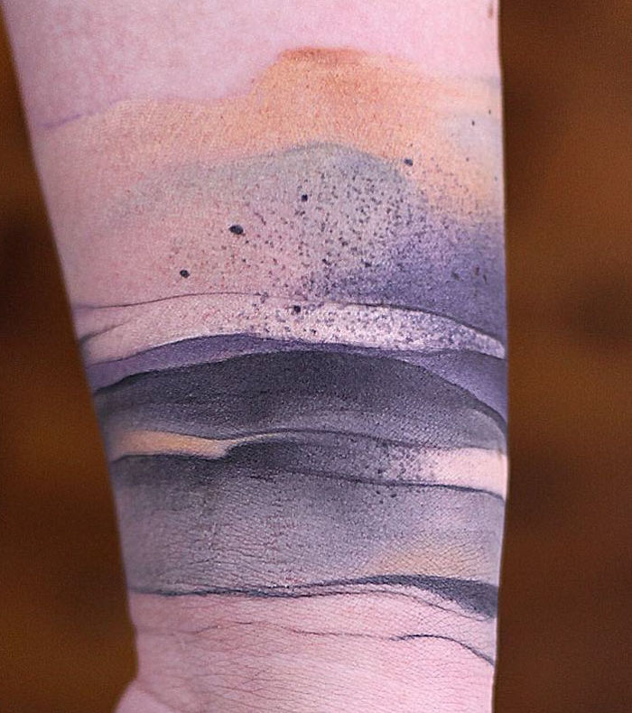 Watercolor tattoo on forearm featuring soft, blended earth tones and abstract design.
