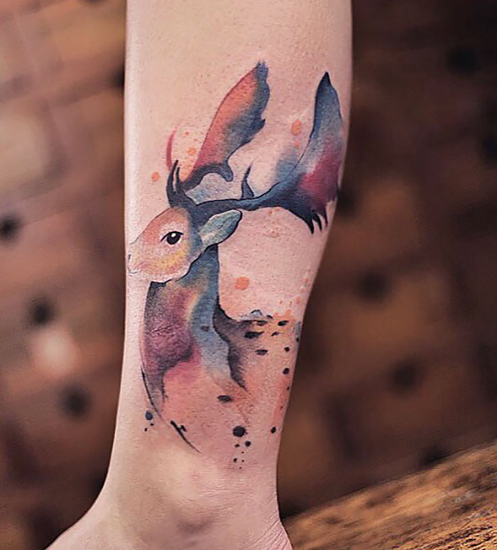 Watercolor tattoo of a colorful deer on forearm, showcasing Chen Jie's artistic style.