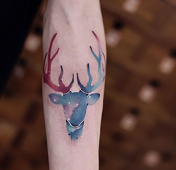 Watercolor tattoo of a colorful deer design on an arm, showcasing Chen Jie's artistic style.