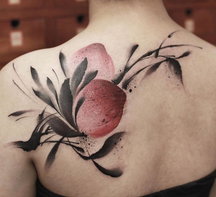 Watercolor tattoo on upper back with floral and abstract design, featuring pink and black hues.