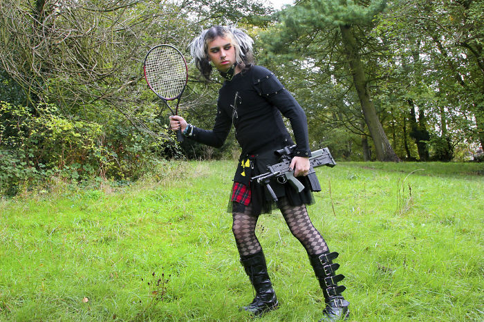 Young goth holding a tennis racket in one hand and gun in another