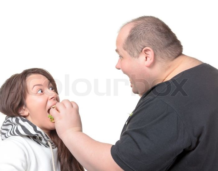 Fat man is feeding a woman with a burger