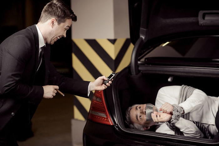 Happy man taking a photo of the other man tied up in a car trunk