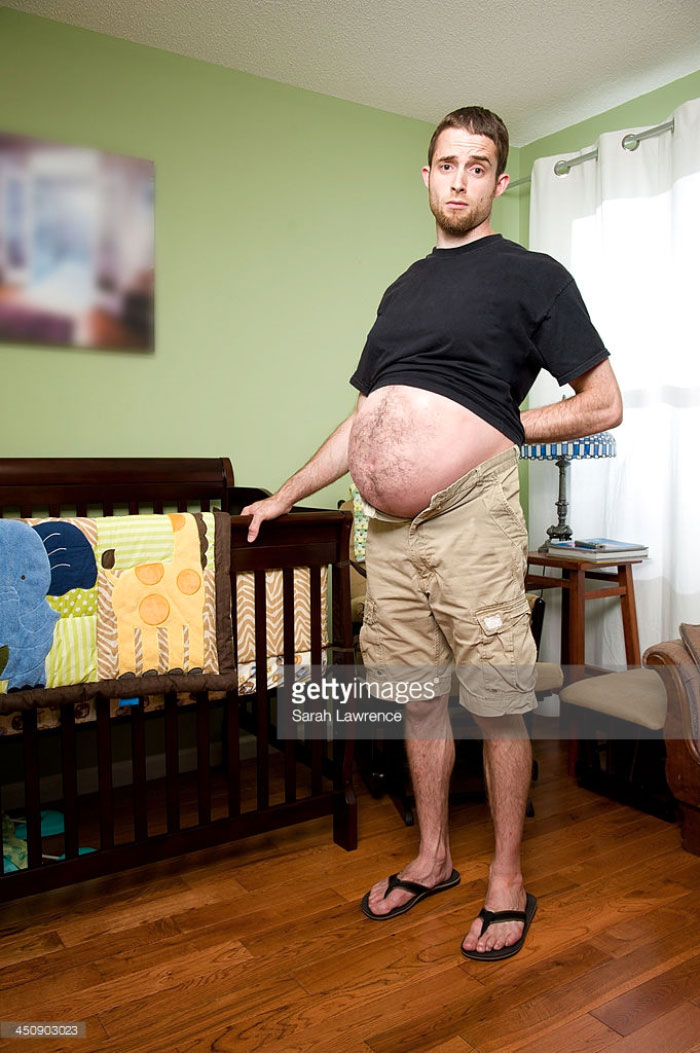 Young man showing his big belly as if he is pregnant