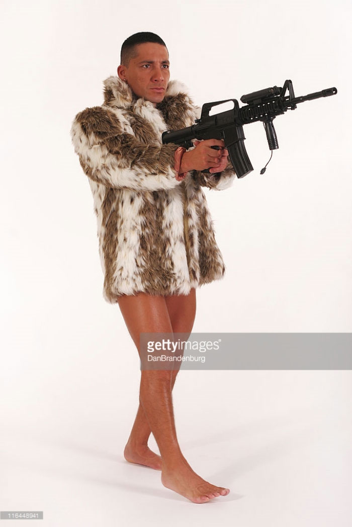 Naked man wears a fur coat and holds the gun in his hands
