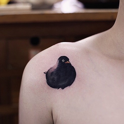 Watercolor tattoo of a black bird on a person's shoulder.