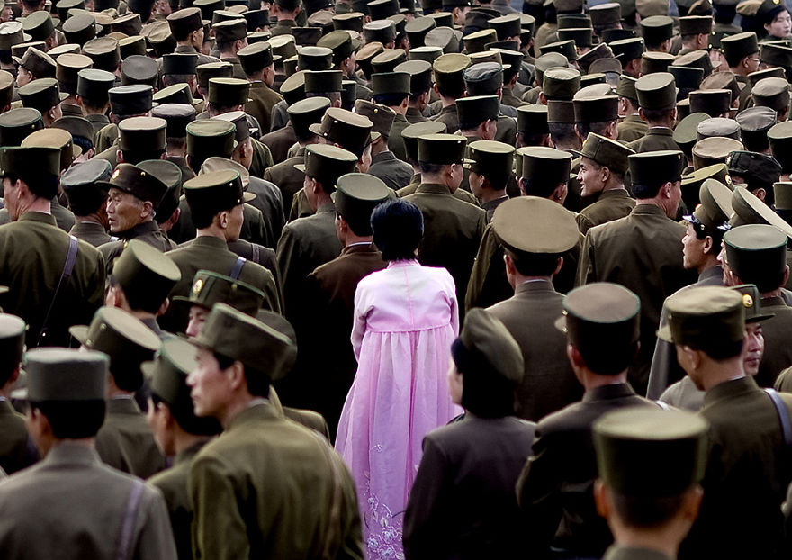 A woman in a pink dress standing in the middle of a crowd of soldiers