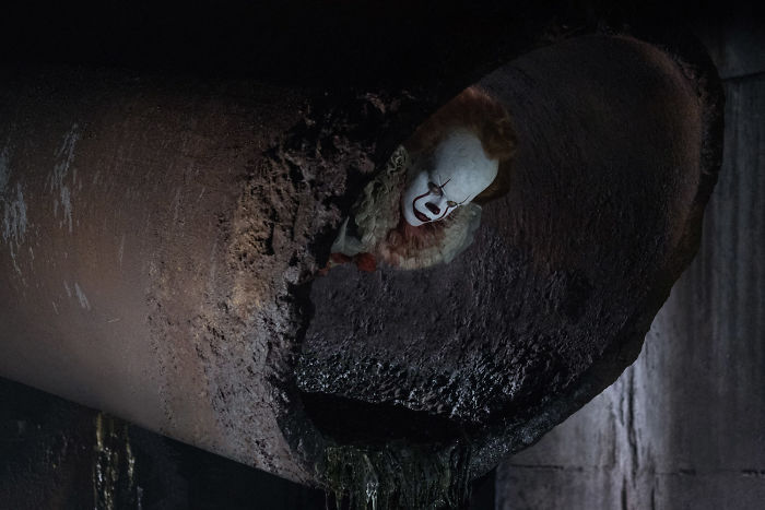 Pennywise the clown lurking inside a large dark sewer pipe in a chilling scene from the It movie horror film.