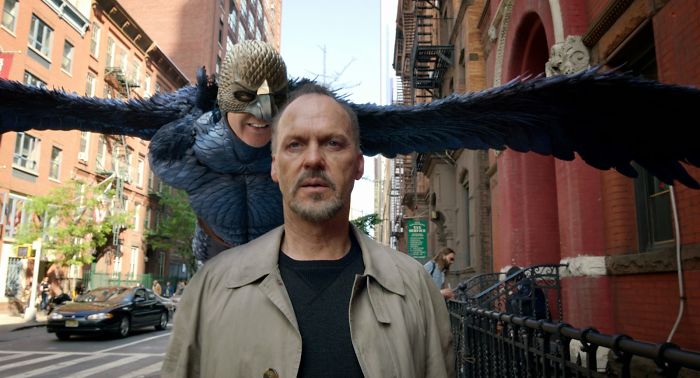 Scene from Birdman movie showing a man in a trench coat with a character in a bird costume behind him on a city street.