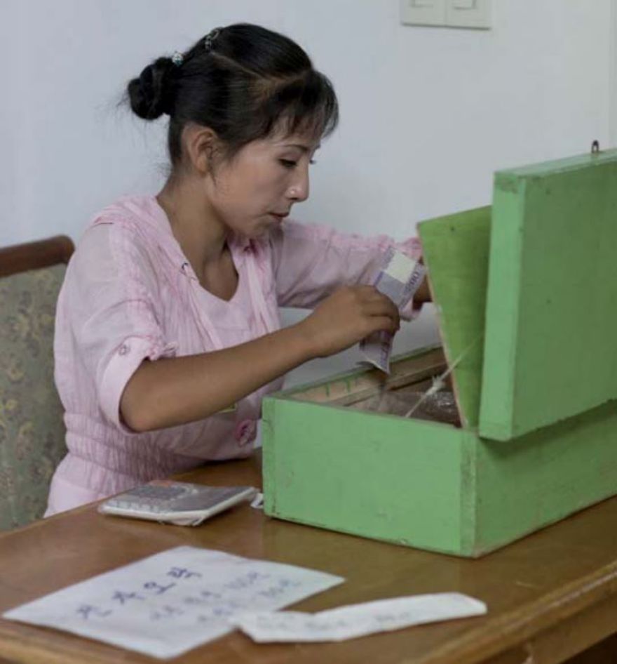 A woman counting money and putting them in the green box 
