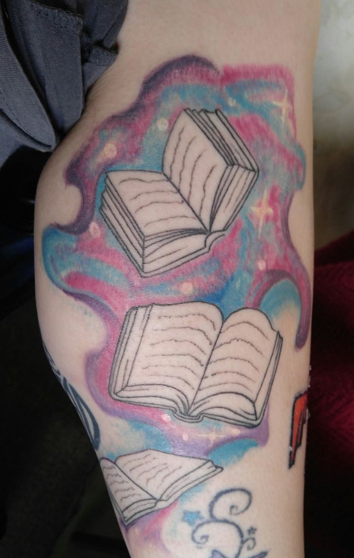 Colorful tattoo of open books with a cosmic background, showcasing personal stories and creativity.