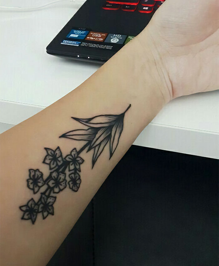 Floral tattoo on forearm near a laptop, showcasing personal stories behind unique tattoos.
