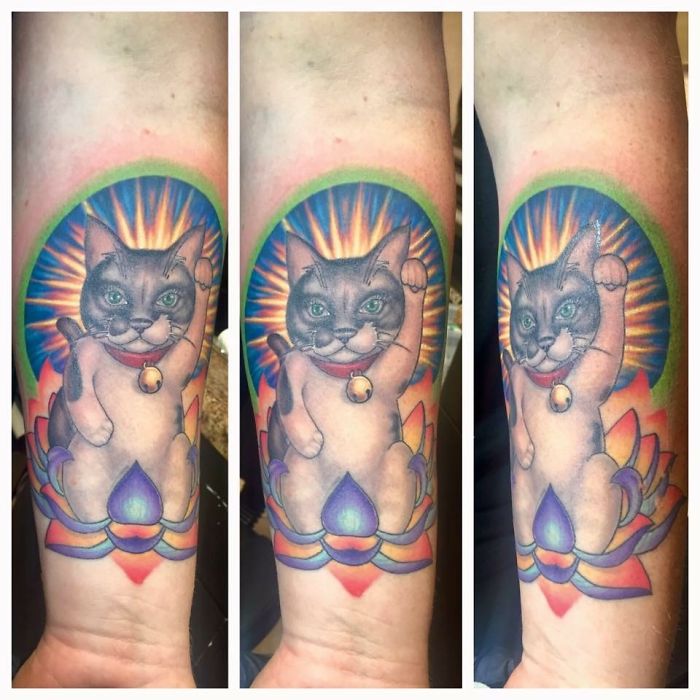 Tattoo of a lucky cat with vibrant colors and a radiant background.