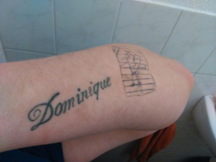 Tattoo of the name "Dominique" and a stick figure drawing on a person's thigh.