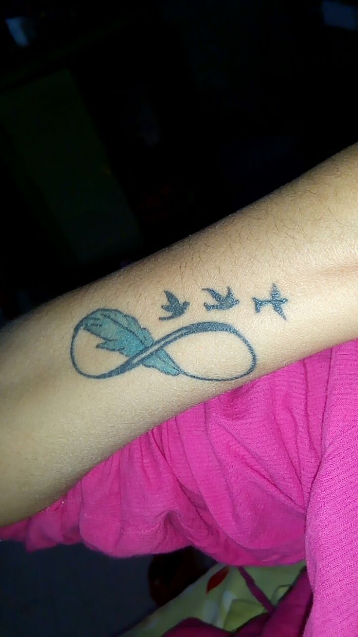 Tattoo of an infinity symbol with birds and a feather, representing personal stories and meanings behind tattoos.
