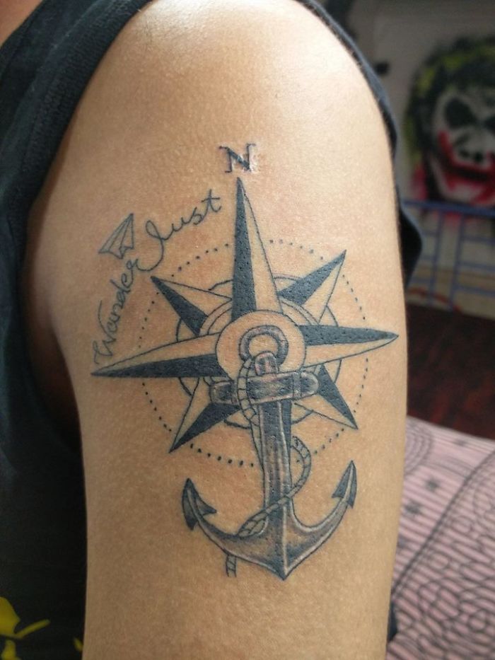 Compass and anchor tattoo on an arm, featuring the words "wanderlust" as part of the design.