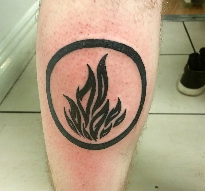 Black flame tattoo inside a circle on a person's leg, showcasing the story behind this unique design.