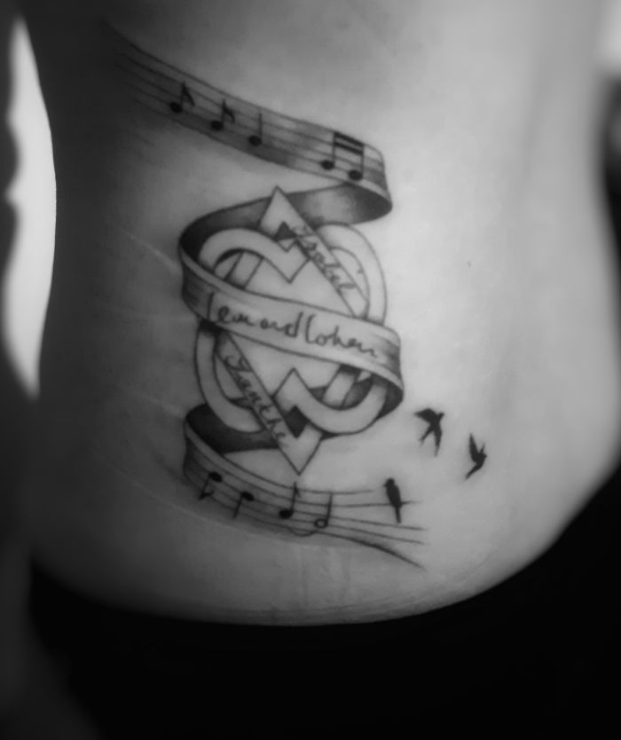 Tattoo featuring music notes, intertwined ribbon with script, and birds; symbolic and personal design.