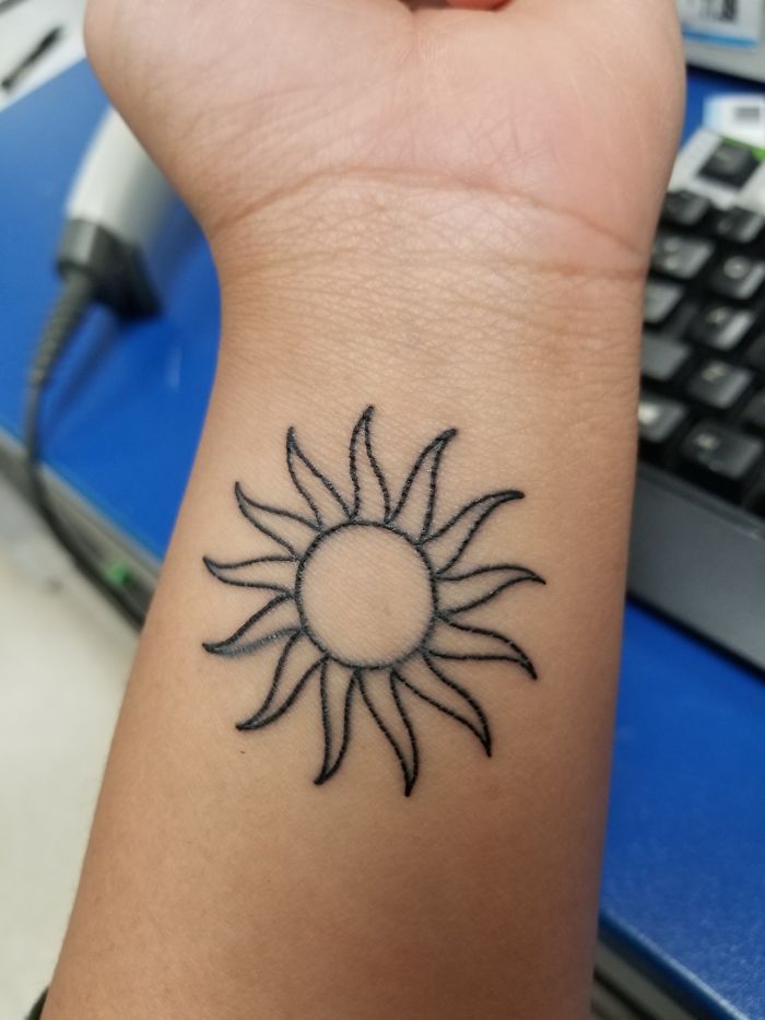Sun tattoo on inner wrist against a blue background, representing personal stories and meaningful tattoos.