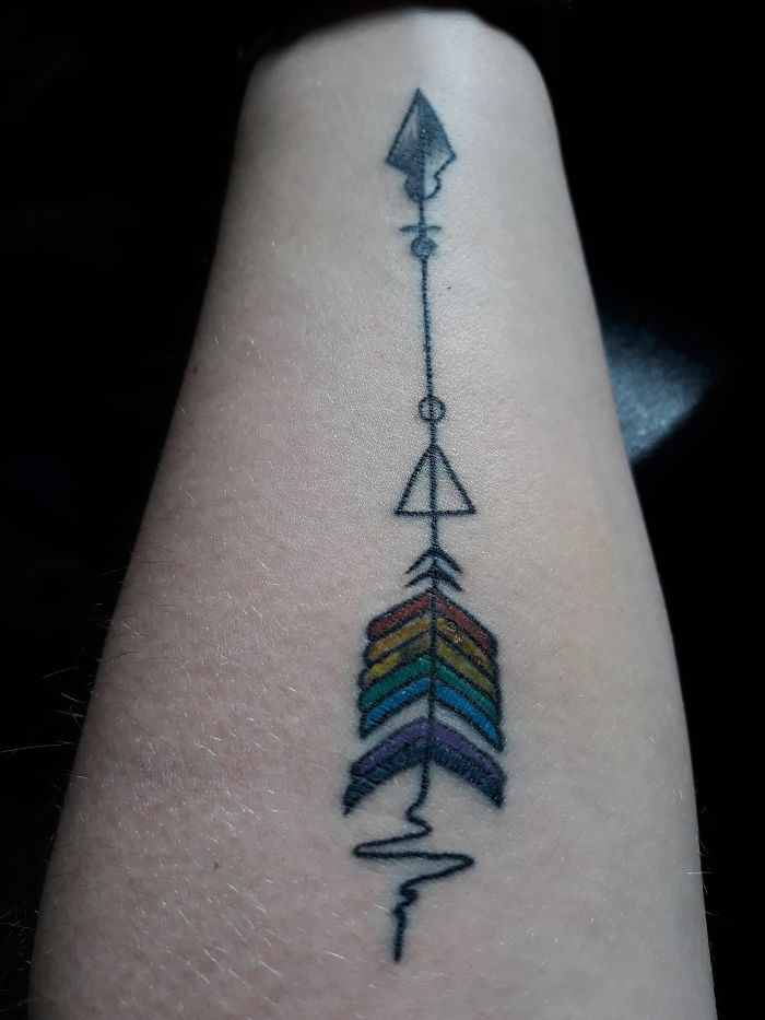 Arrow tattoo with geometric shapes and rainbow feathers on forearm, highlighting personal stories behind tattoos.
