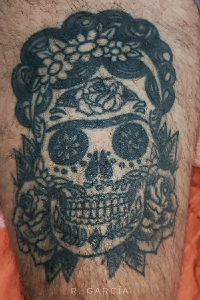 Tattoo of a skull adorned with flowers and intricate designs on leg.