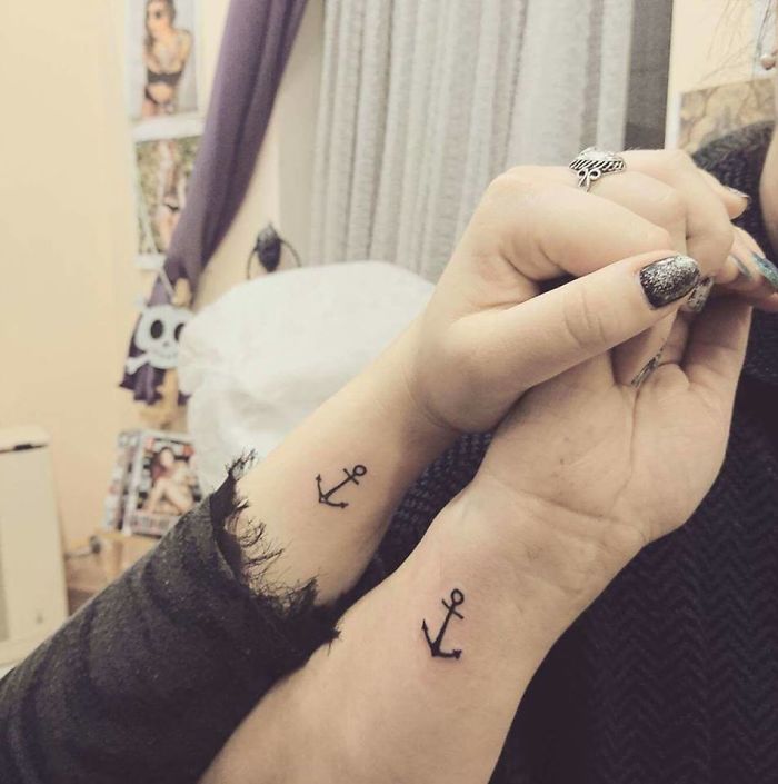 Two wrists with matching anchor tattoos, symbolizing shared stories and connection.