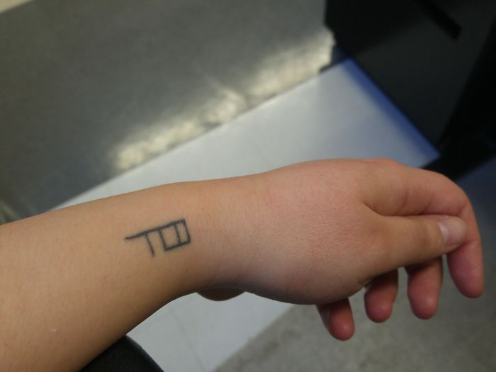 A small minimalist tattoo on a person's wrist, featuring a simple design with lines and shapes.
