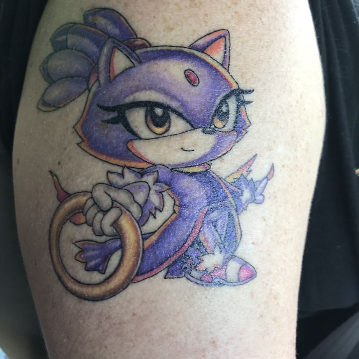 Colorful cartoon cat tattoo with a ring on an arm, showcasing personal tattoo stories.