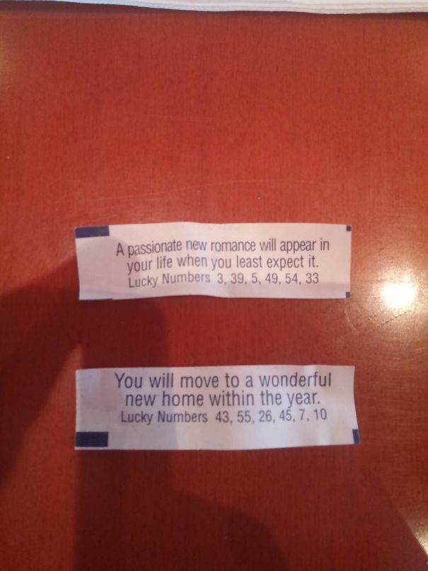 Fortune cookie sayings predicting romance and a new home, placed on a wooden table.