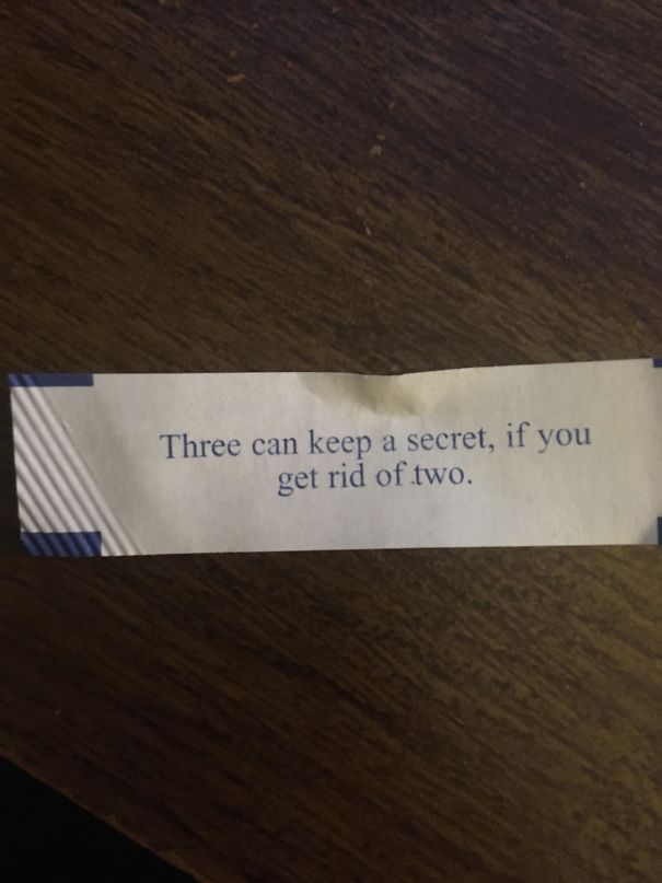 Fortune cookie saying: "Three can keep a secret, if you get rid of two," on a wooden table.