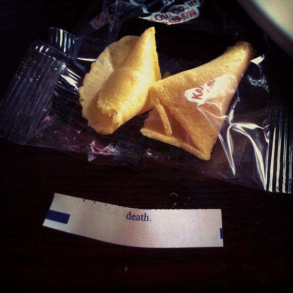 Open fortune cookie with a sassy fortune message about death on a table.