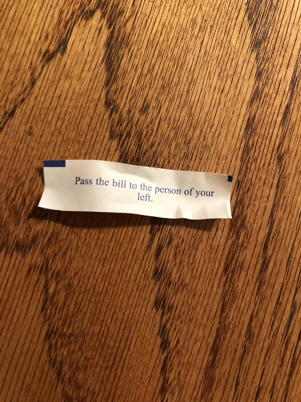 Fortune cookie saying on a wooden table reading, "Pass the bill to the person of your left," with a sassy tone.