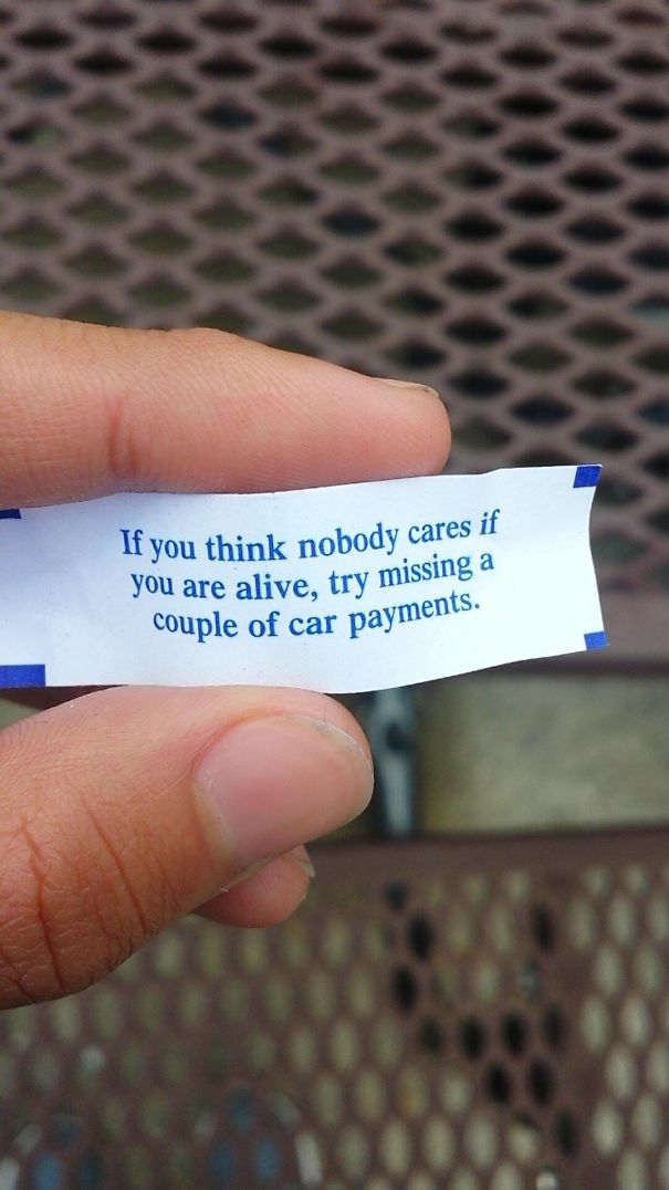 Sassy fortune cookie message about missing car payments, held between fingers.