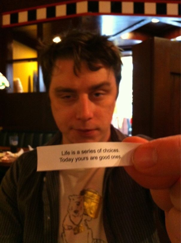Man holding a sassy fortune cookie saying, "Life is a series of choices. Today yours are good ones," in a restaurant setting.